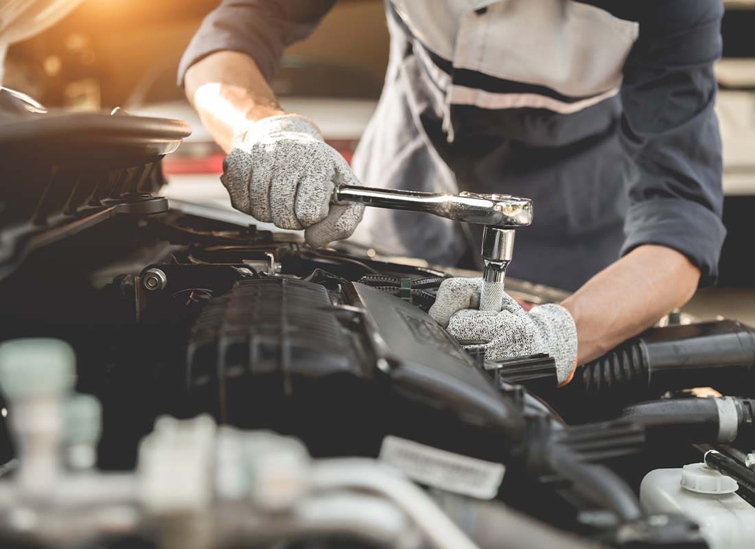 Garage Repair Shop Insurance - Auto Mechanic Working with His Hands and Servicing a Car and Repairing the Engine in the Automotive Workshop with a Wrench